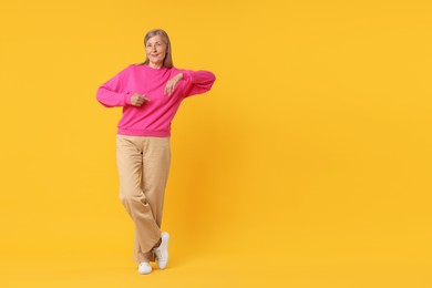 Photo of Happy senior woman pointing on orange background, space for text