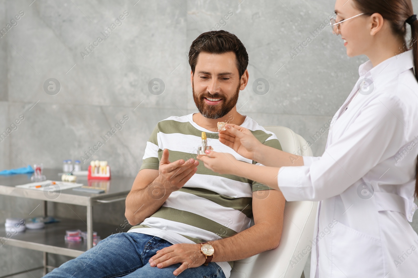 Photo of Doctor with educational model of dental implant consulting patient in clinic