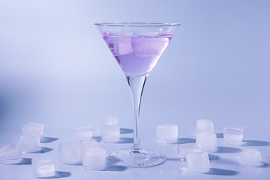 Fresh cocktail in martini glass with ice cubes on light blue background