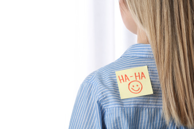 Photo of Woman with HA-HA sticker on back against light background, closeup. April Fool's Day