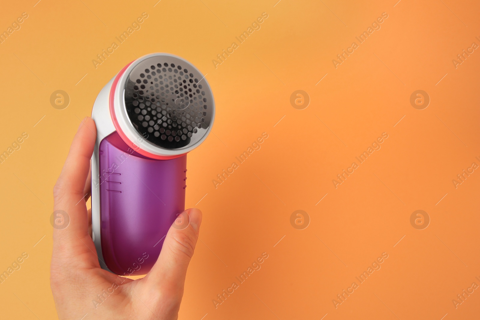 Photo of Woman holding modern fabric shaver on pale orange background, closeup. Space for text