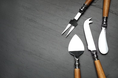 Cheese knives and fork on black stone table, flat lay. Space for text