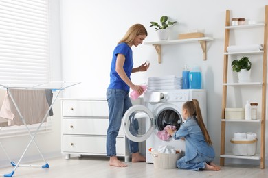 Photo of Mother pouring fabric softener while daughter putting dirty clothes into washing machine in bathroom, space for text