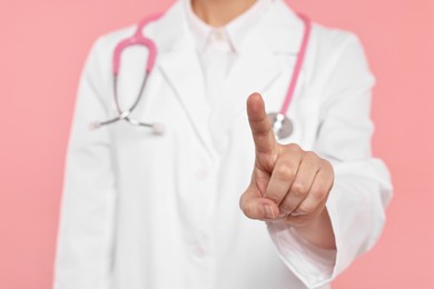 Doctor with stethoscope pointing on pink background, closeup