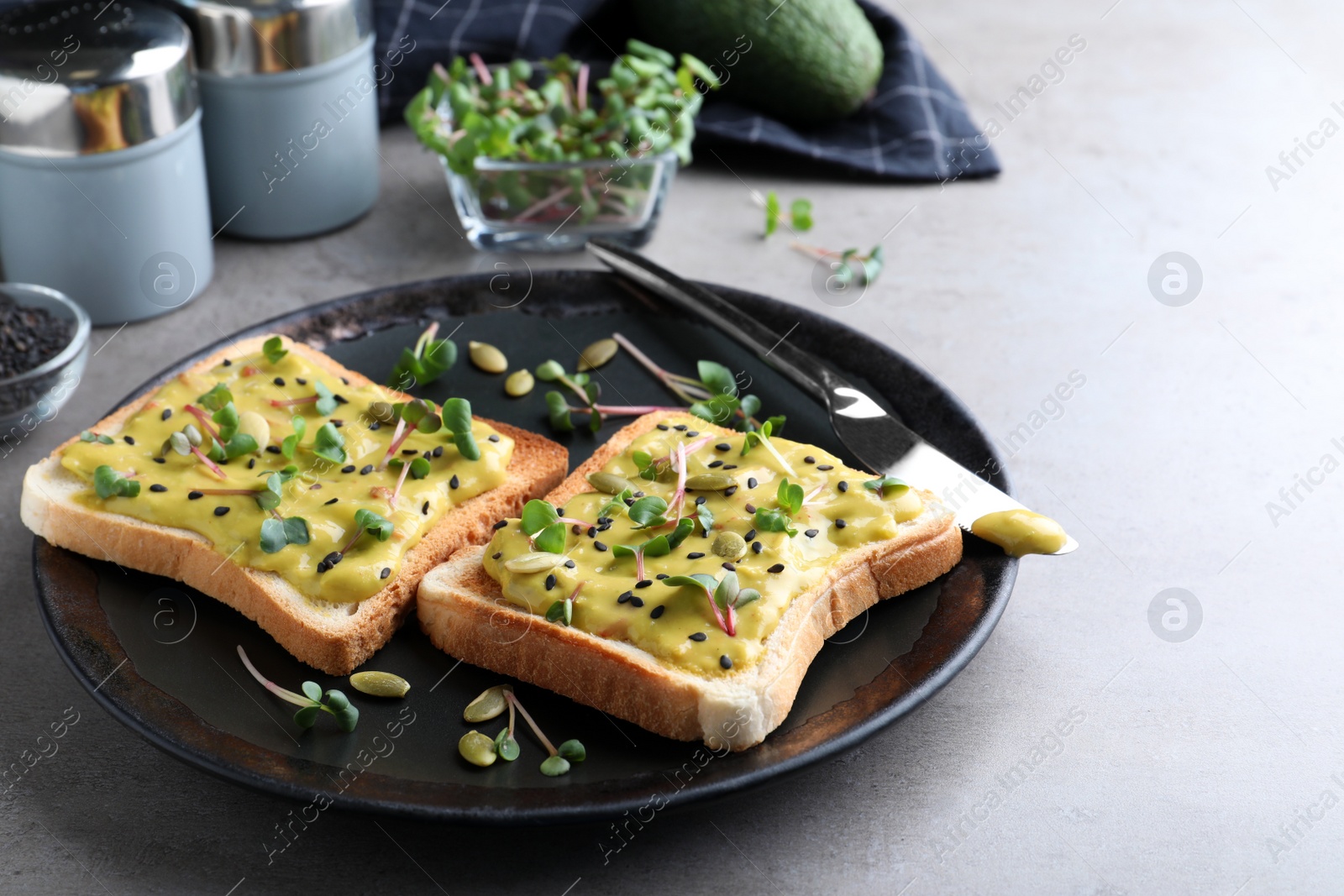 Photo of Delicious sandwiches with guacamole, seeds and microgreens on grey table