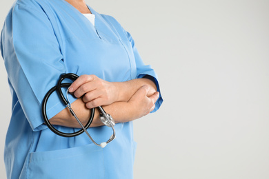 Mature doctor with stethoscope on light grey background, closeup. Space for text