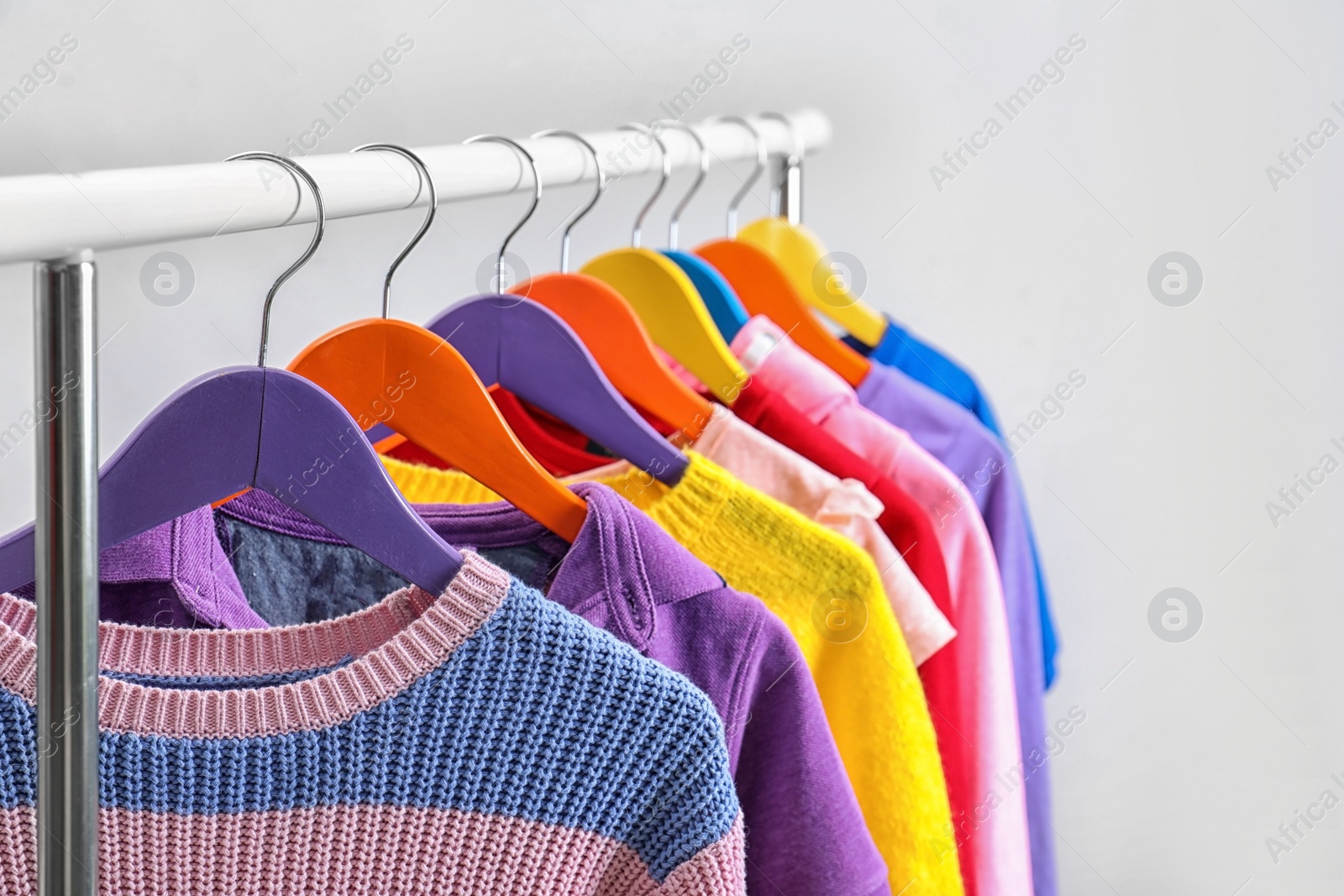 Photo of Colorful clothes hanging on wardrobe rack against light background, closeup