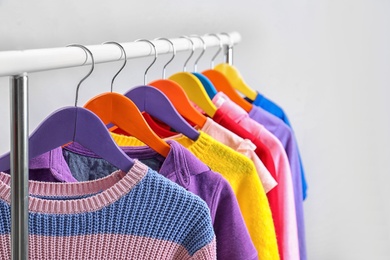 Colorful clothes hanging on wardrobe rack against light background, closeup