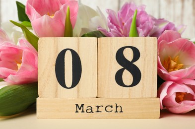 Block calendar with date 8th of March and tulips on table against wooden background. International Women's Day