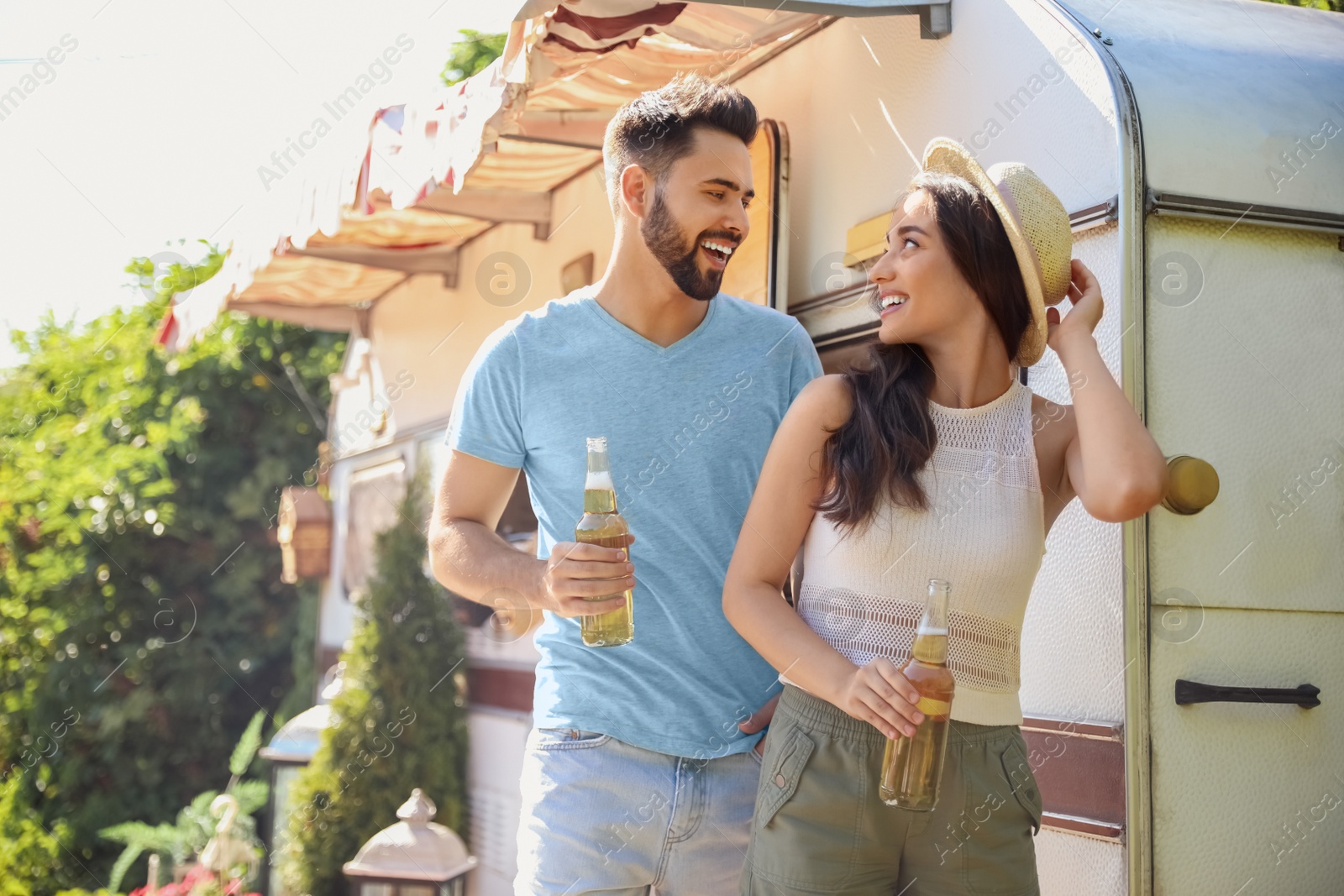 Photo of Happy couple with bottles of beer near motorhome. Camping season