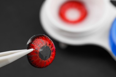 Photo of Tweezers with red contact lens on dark background, closeup. Space for text