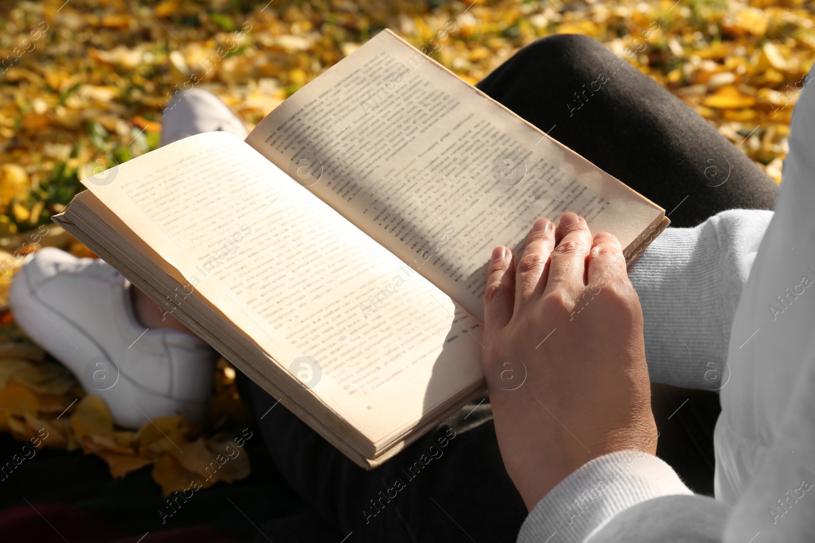 Photo of Woman reading book outdoors on autumn day, closeup