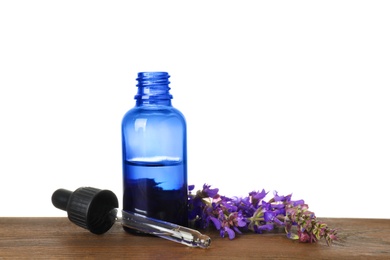 Photo of Bottle of herbal essential oil, pipette and sage flowers on wooden table, white background