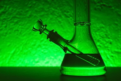 Photo of Glass bong on table, toned in green. Smoking device