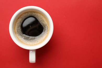 Fresh coffee in cup on red background, top view. Space for text