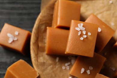 Yummy caramel candies and sea salt on black table, closeup