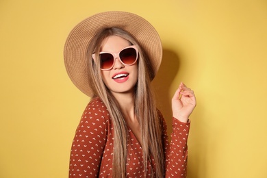 Photo of Young woman wearing stylish sunglasses and hat on yellow background