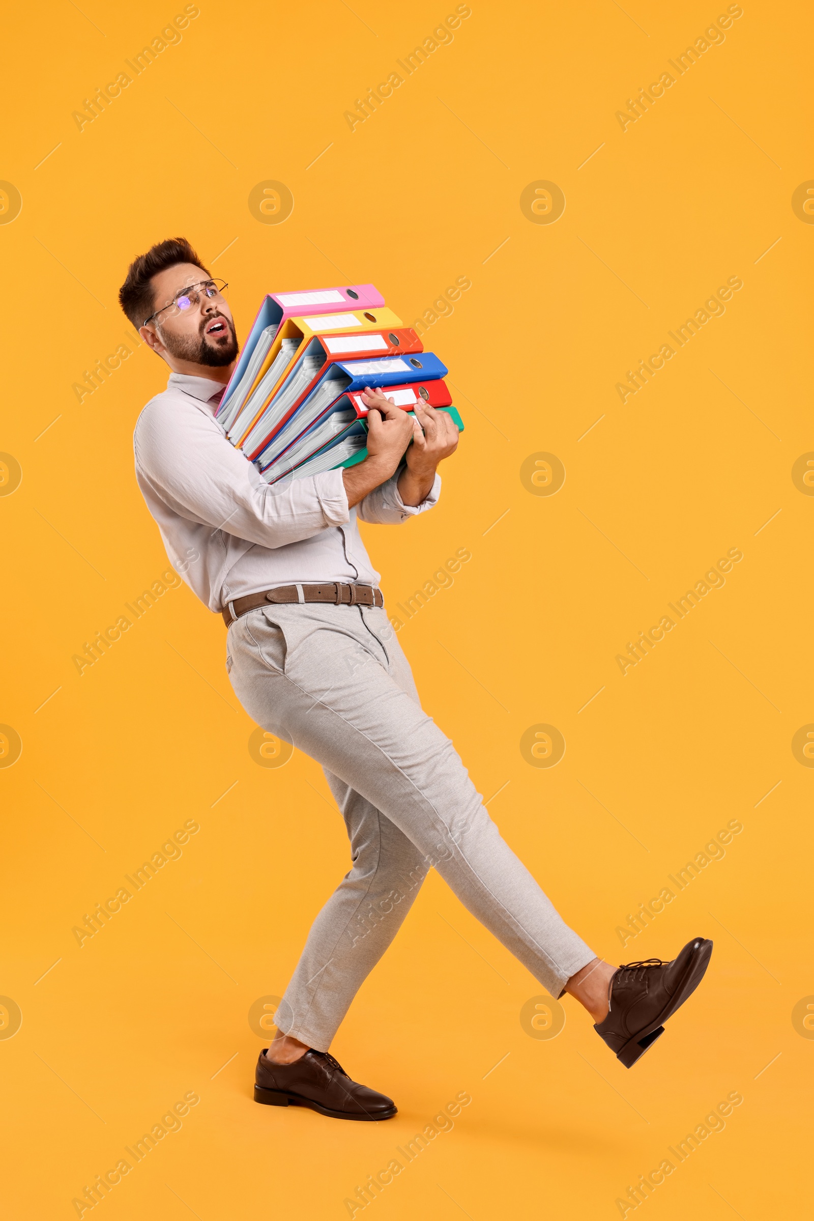 Photo of Stressful man with folders walking on orange background