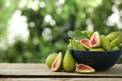 Photo of Cut and whole green figs on wooden table against blurred background, space for text