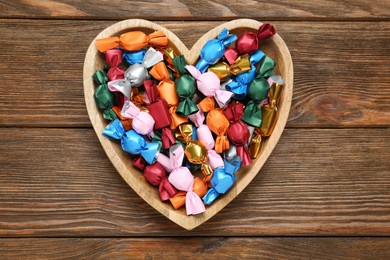 Heart shaped plate with candies in colorful wrappers on wooden table, top view