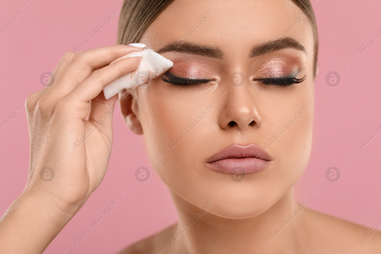 Photo of Beautiful woman removing makeup with cotton pad on pink background, closeup