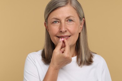 Photo of Senior woman taking pill on beige background