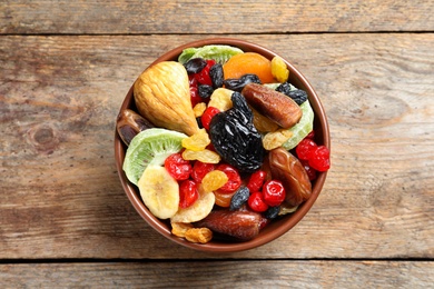 Photo of Bowl with different dried fruits on wooden background, top view. Healthy lifestyle