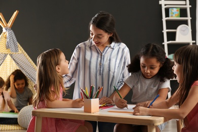 Photo of Cute little children with nursery teacher drawing at table in kindergarten. Indoor activity