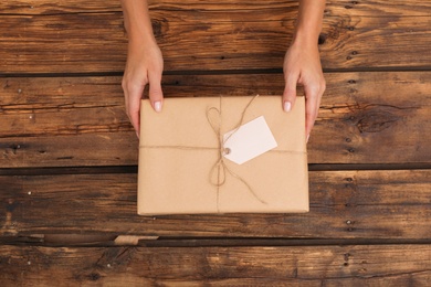 Woman holding parcel with tag on wooden background, top view