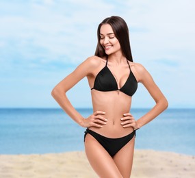 Happy woman in stylish black bikini on sandy beach near sea