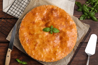 Photo of Delicious pie with meat and basil on wooden table, flat lay