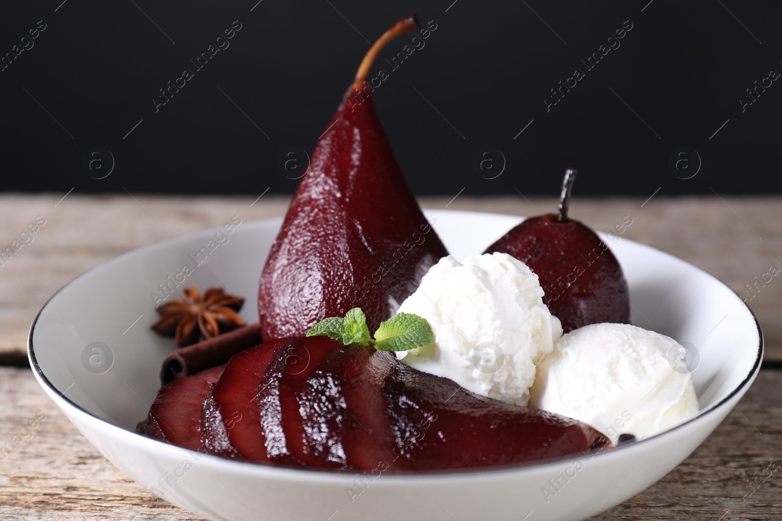 Photo of Tasty red wine poached pears and ice cream in bowl on wooden table, closeup