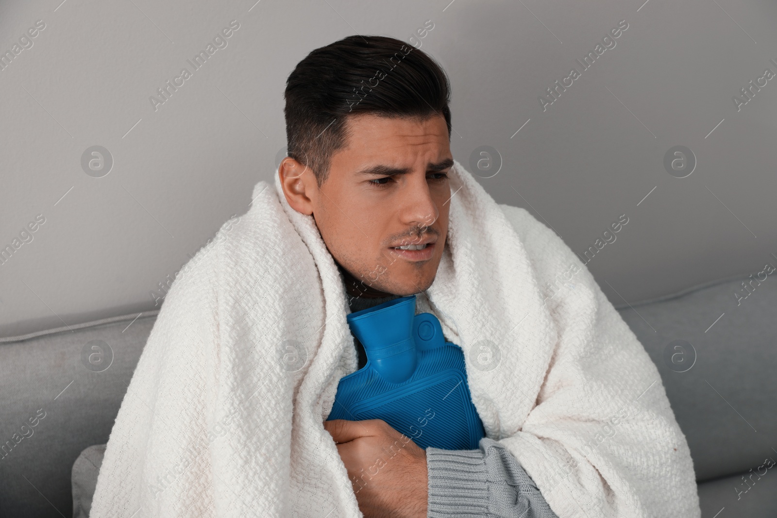 Photo of Ill man with hot water bottle suffering from cold at home