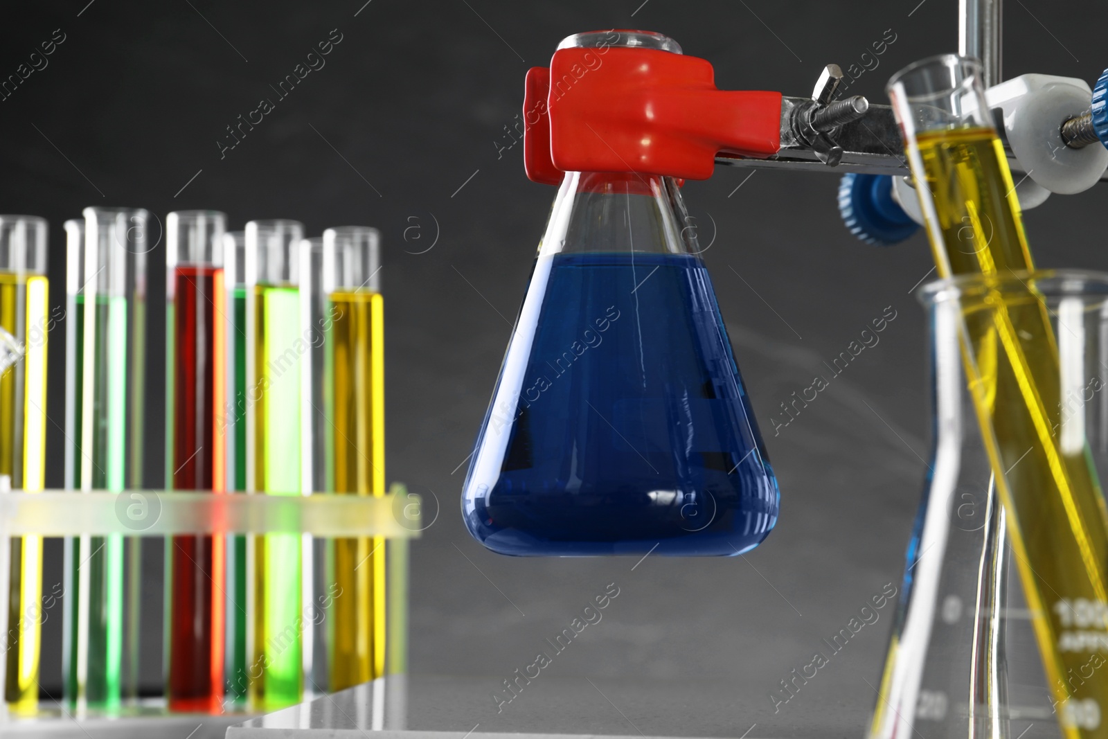 Photo of Retort stand and laboratory glassware with liquids on grey background, closeup