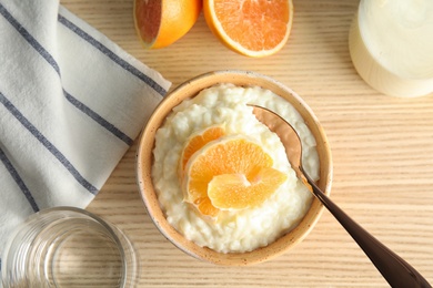 Photo of Creamy rice pudding with orange slices in bowl served on wooden table, top view