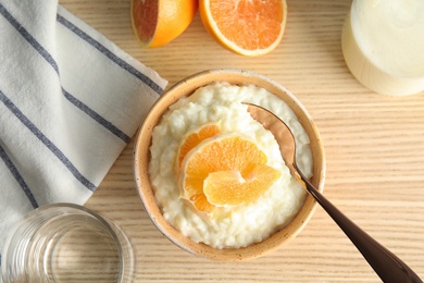 Creamy rice pudding with orange slices in bowl served on wooden table, top view