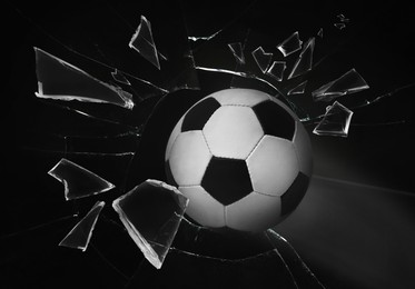 Soccer ball breaking up glass against black background