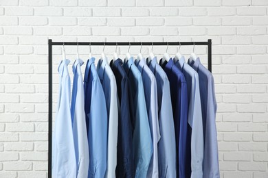 Dry-cleaning service. Many different clothes hanging on rack against white brick wall