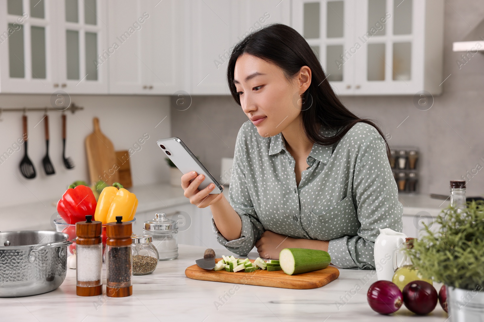 Photo of Beautiful woman with smartphone cooking in kitchen