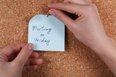 Woman pinning paper note with phrase Meeting On Friday to cork board, closeup