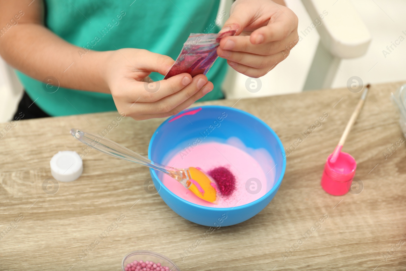 Photo of Little girl making homemade slime toy at table, closeup