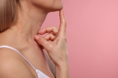 Woman touching her neck on pink background, closeup. Space for text