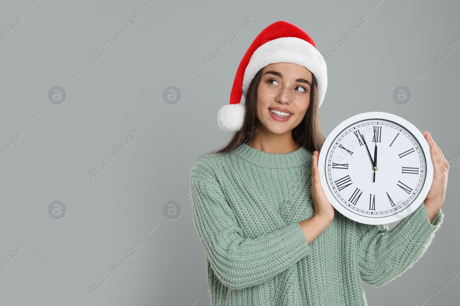 Photo of Woman in Santa hat with clock on grey background, space for text. New Year countdown