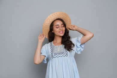 Beautiful young woman with straw hat on light grey background
