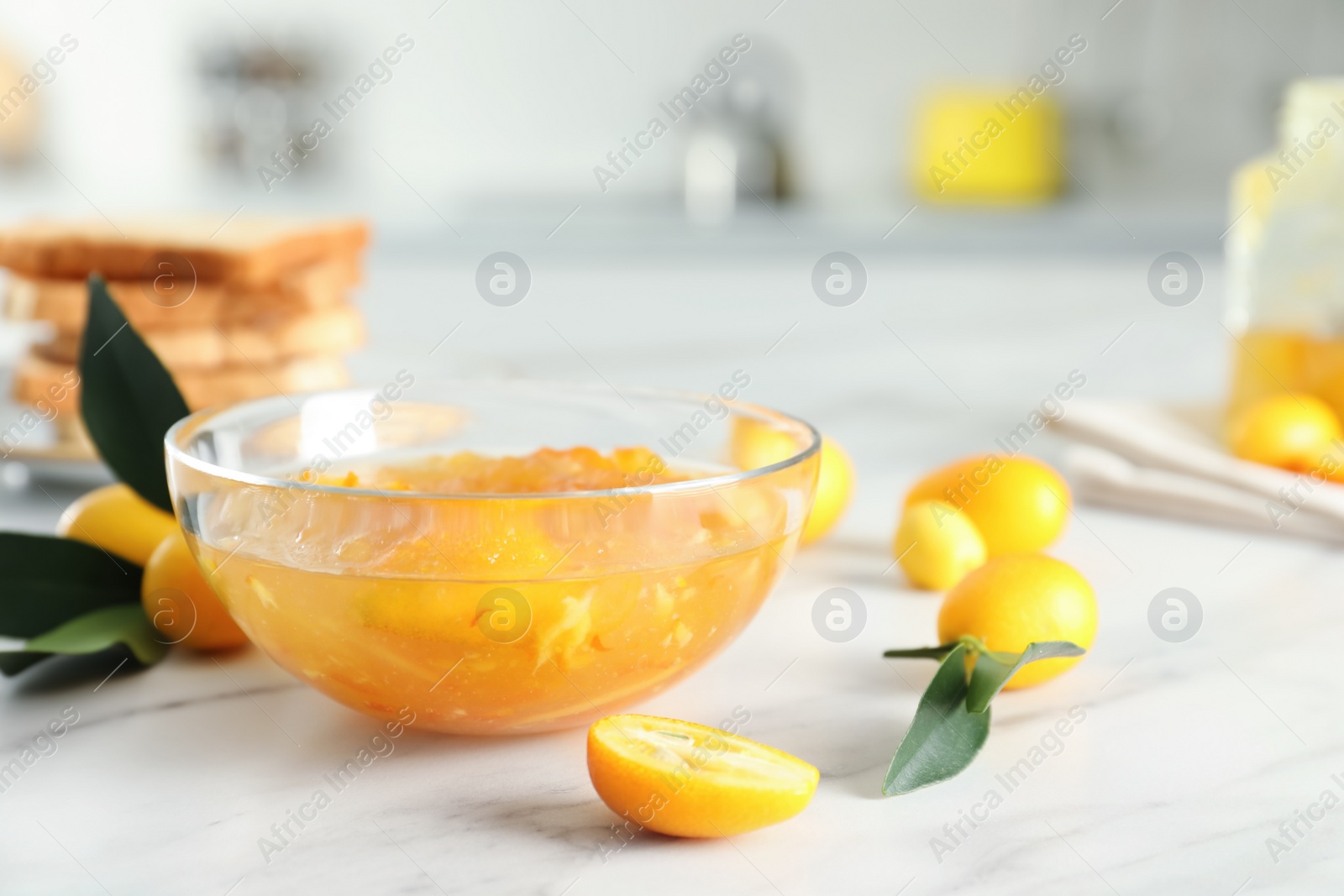 Photo of Delicious kumquat jam and fresh fruits on white marble table