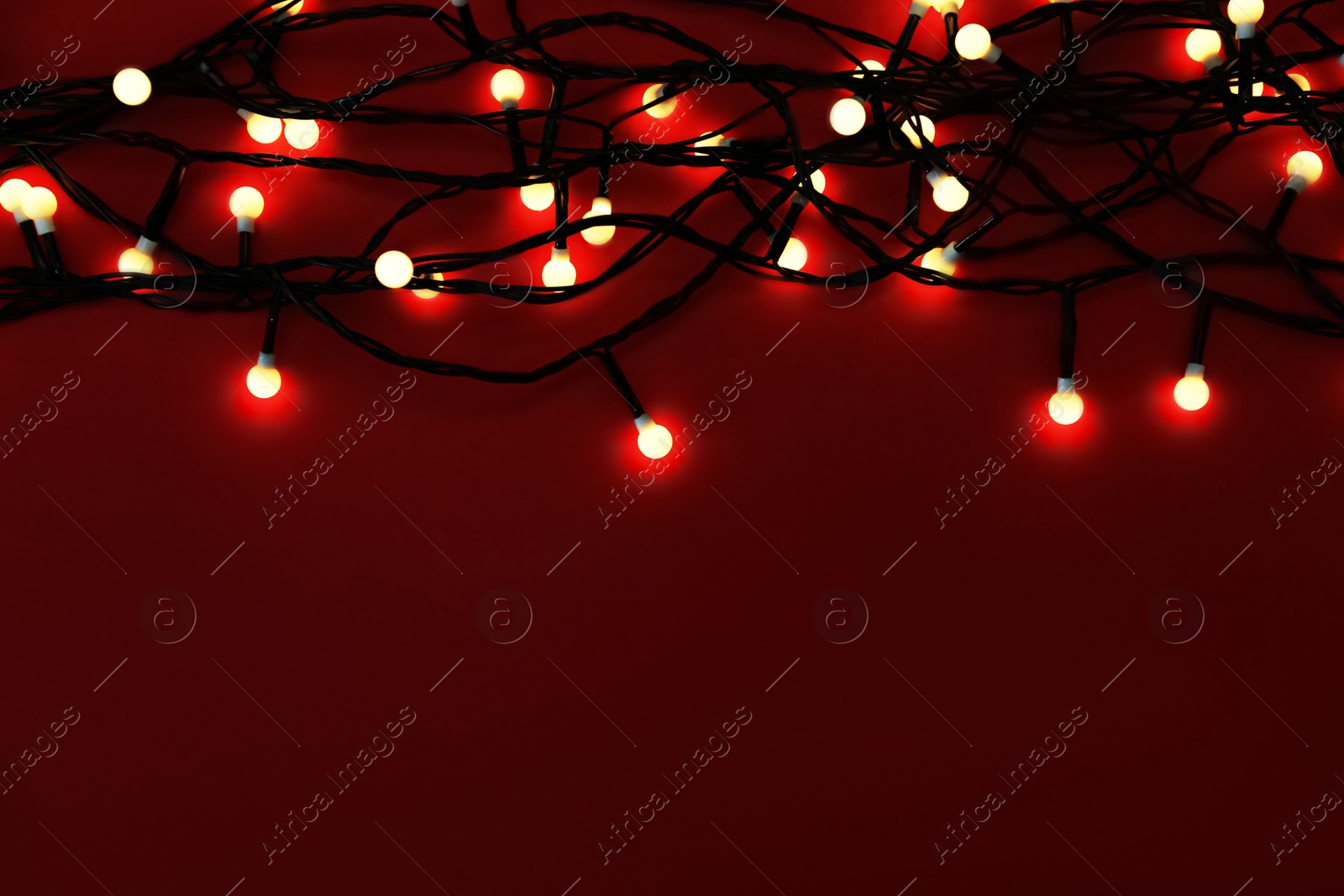 Photo of Glowing Christmas lights on red background, top view. Space for text