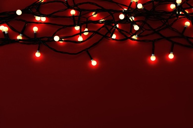 Glowing Christmas lights on red background, top view. Space for text