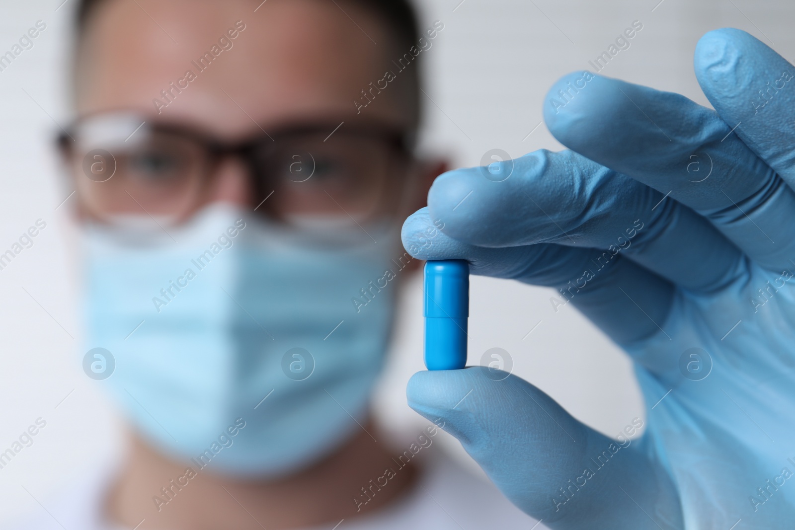 Photo of Doctor holding pill on light background, selective focus. Space for text