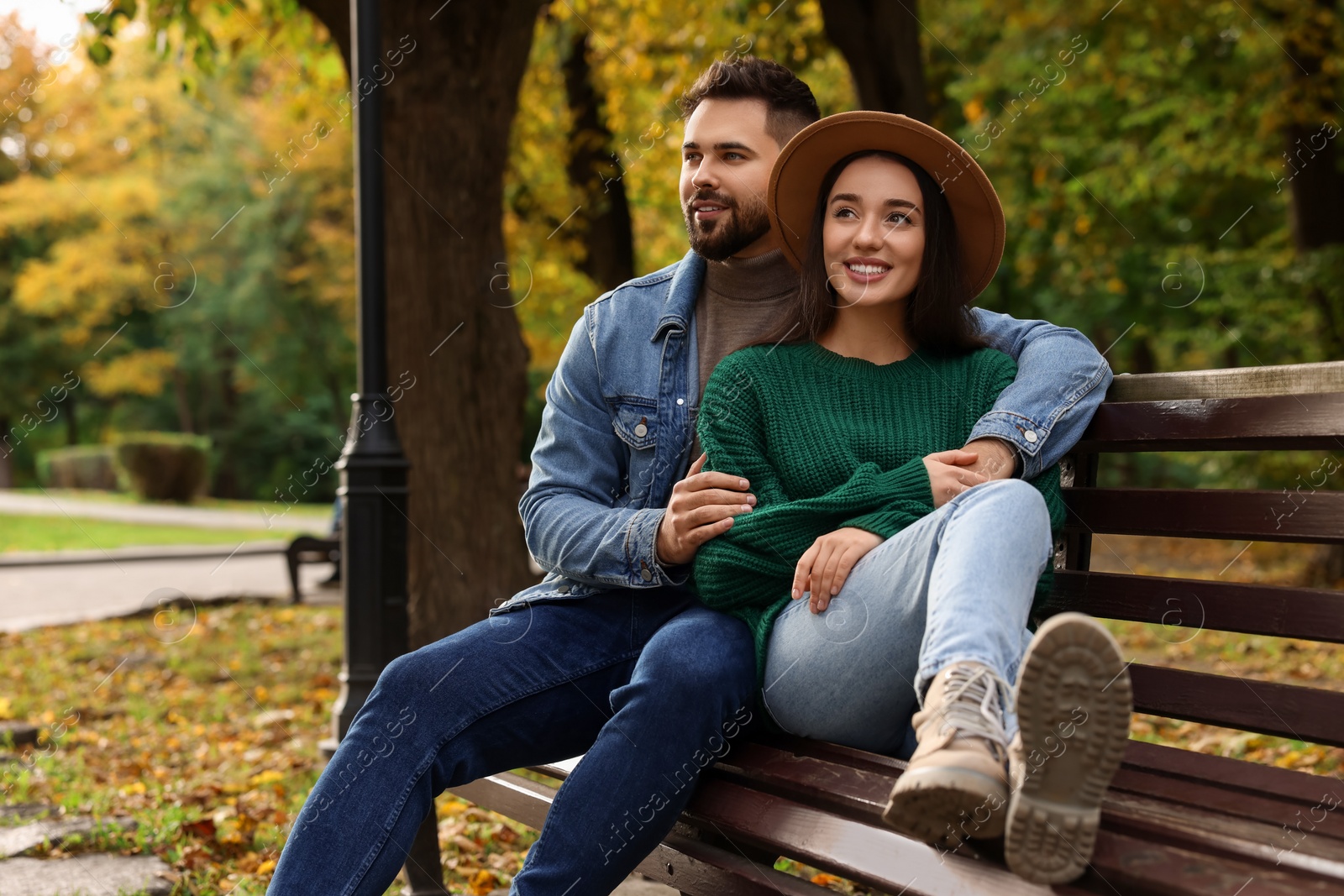 Photo of Happy young couple spending time together on wooden bench in autumn park, space for text