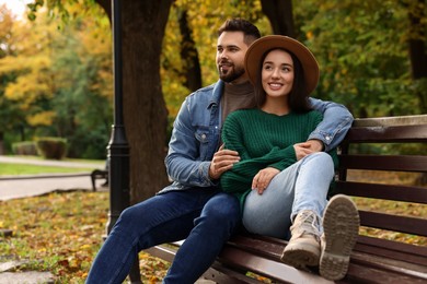 Happy young couple spending time together on wooden bench in autumn park, space for text